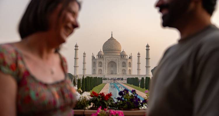 Soft-focused couple admire the Taj Mahal from a rooftop garden lined with flowers at dawn.