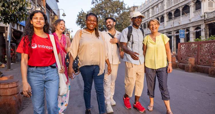 A diverse group of travelers walk and laugh along a busy street lined with historic buildings in Delhi.