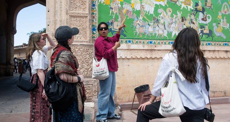 Guide gestures toward a vibrant historical mural inside an ornate Indian fort while tourists listen.
