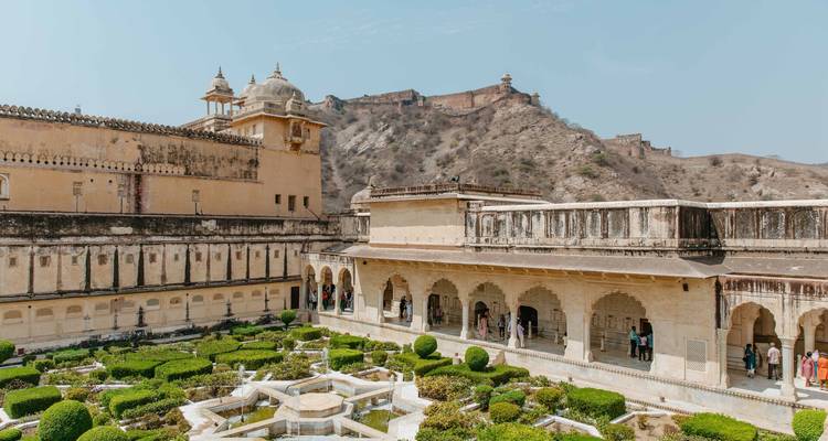 The symmetrical gardens and sandstone arches of Amber Fort sit below rugged hills under a pale blue sky.