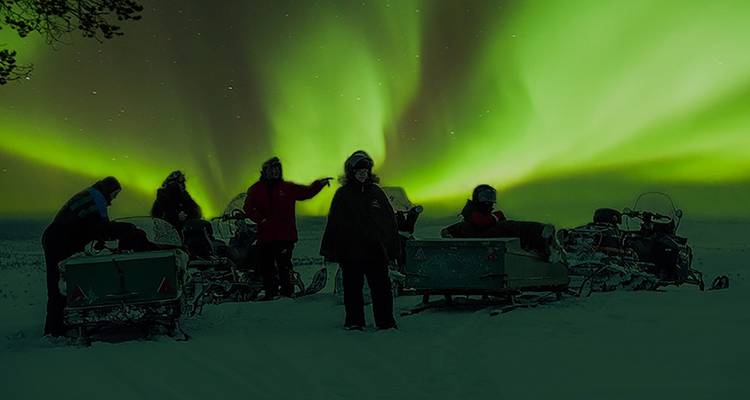 Mensen op sneeuwscooters met noorderlicht aan de hemel.