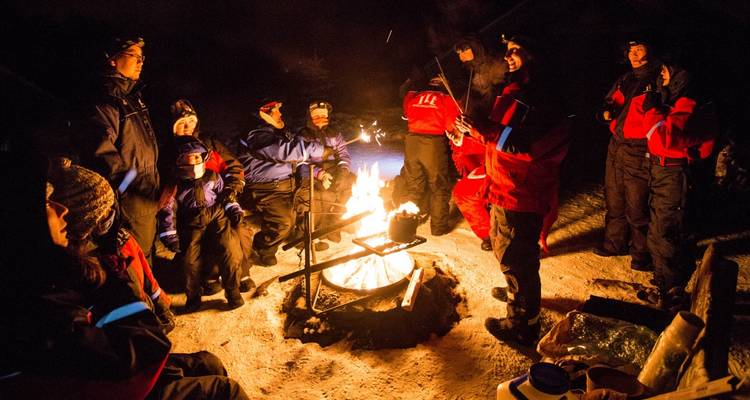 Groep mensen die 's nachts bij een kampvuur zitten.
