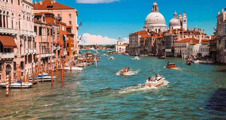 Des bateaux naviguent le long du Grand Canal de Venise en direction des dômes de la Basilique Santa Maria della Salute sous un ciel bleu éclatant.