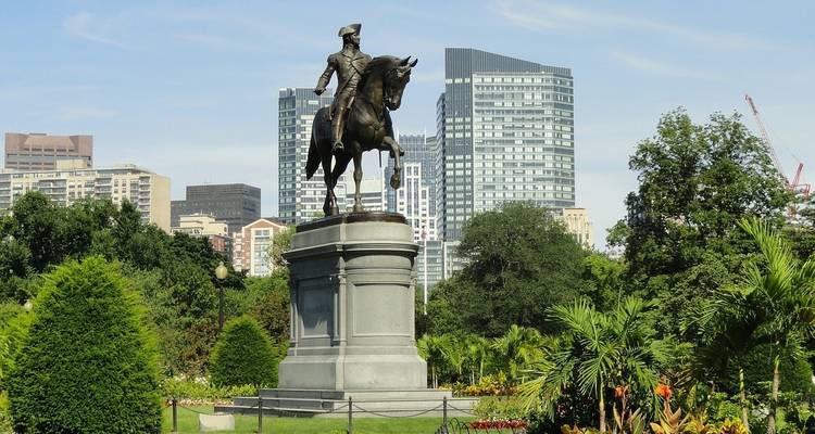 Estatua ecuestre en un parque público con edificios de la ciudad al fondo.