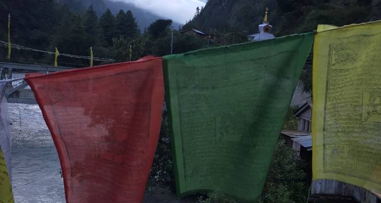 Las banderas de oración ondeando sobre un río que fluye rápidamente al atardecer con colinas brumosas al fondo.