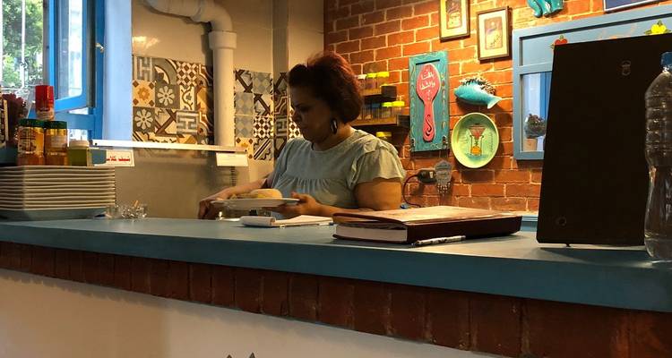 Een persoon die achter een toonbank werkt in een restaurant met een bakstenen muur en kleurrijke tegels.