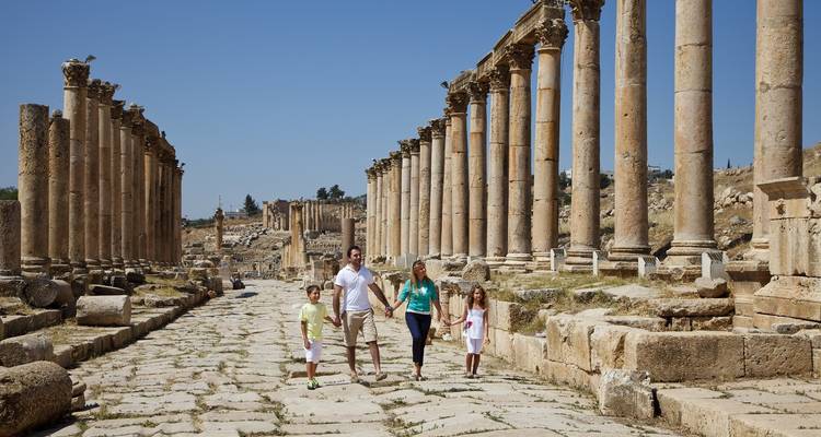 Familia caminando entre columnas romanas antiguas que bordean una calle empedrada.