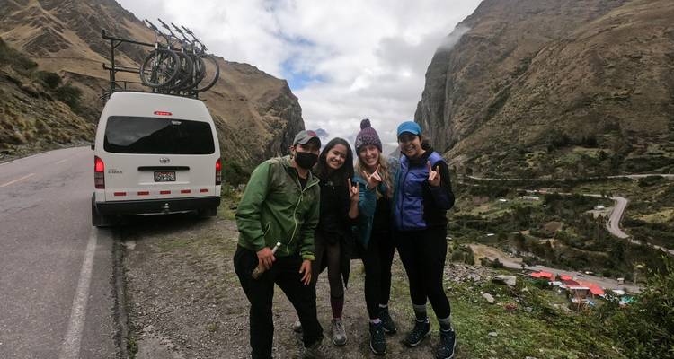 Un grupo de amigos posando junto a una furgoneta con bicicletas en una carretera de montaña.