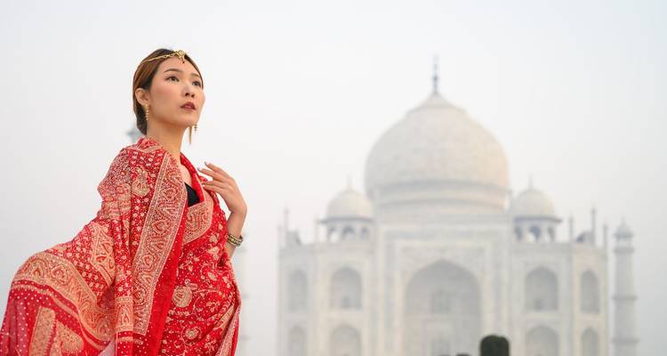 Elegante Frau in roter traditioneller Kleidung, die vor dem sanft unscharfen Taj Mahal posiert.