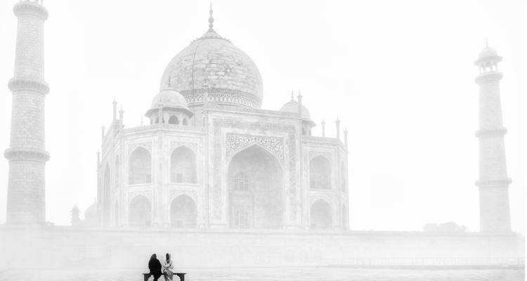 Schwarzweiße minimalistische Szene eines Paares, das allein in der Nähe des nebligen Taj Mahal sitzt.