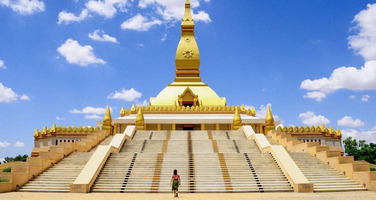 Grand golden Pha That Luang stupa rises above a monumental stairway under bright blue skies.