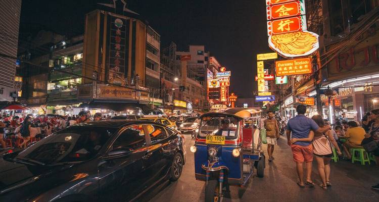 Bustling Bangkok Chinatown at night with neon signs, tuk-tuks and dense traffic.