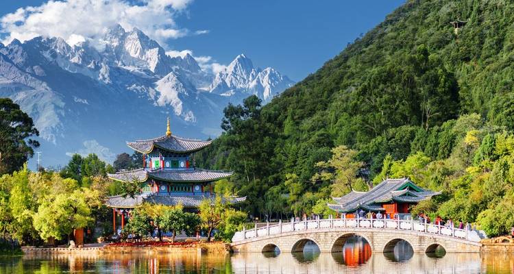 Classical Chinese pavilion by a reflective lake with snow-clad peaks towering behind.