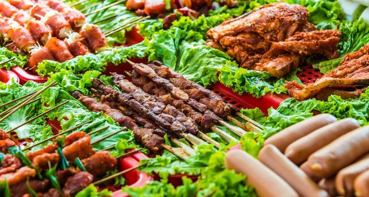 Colorful array of grilled meats and sausages laid out on fresh lettuce at a market stall.