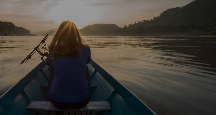 Eine Frau in einem Boot mit Blick auf einen Sonnenuntergang auf einem Fluss.