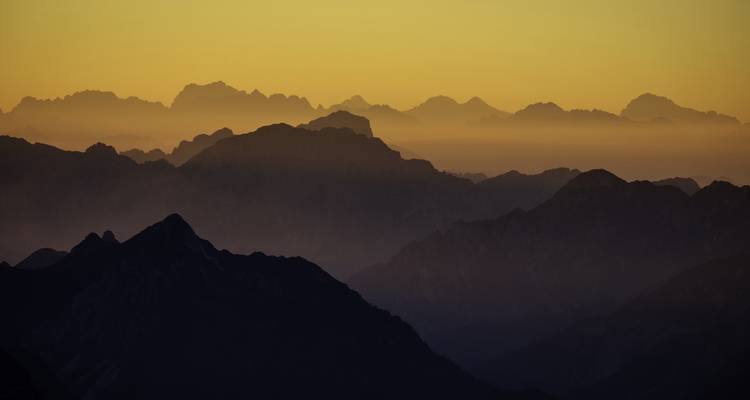 Silhouettes de chaînes de montagnes sous un ciel doré au coucher du soleil.