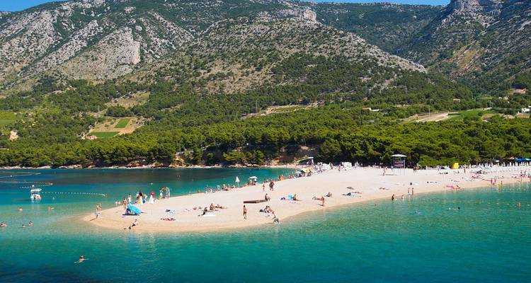 Plage de sable avec des touristes profitant du soleil dans une baie pittoresque.