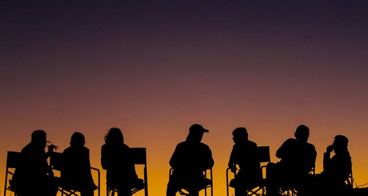 Siluetas de personas sentadas conversando al atardecer.