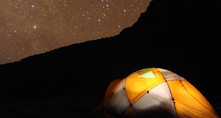Una tienda brillante bajo un cielo nocturno lleno de estrellas en las laderas oscuras del Kilimanjaro.