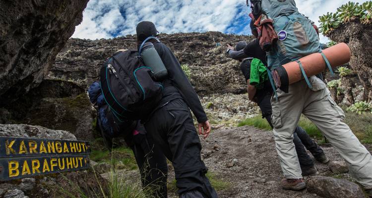 Les trekkers gravissent un sentier abrupt près d'un panneau en bois indiquant le refuge de Karanga et le refuge de Barafu sur le Kilimandjaro.