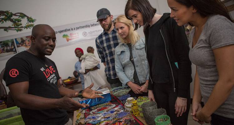 Travellers listen to a local artisan explaining colourful handmade crafts laid out on a table.