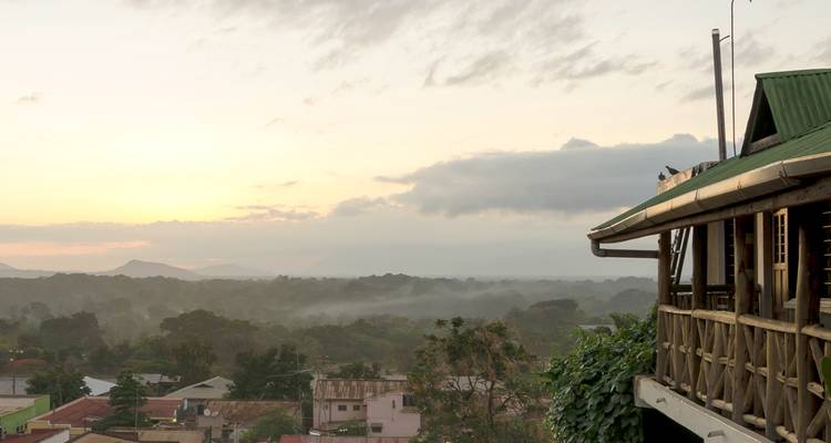 Luz suave del amanecer sobre bosque brumoso y colinas lejanas vistas desde el balcón de una cabaña de madera.