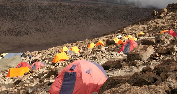 Tiendas de color naranja brillante y amarillo salpican un campamento alpino empinado y rocoso en las laderas del Kilimanjaro.