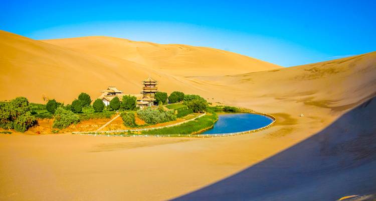 The crescent-shaped oasis lake at Dunhuang’s Crescent Moon Spring nestles amid vast golden desert dunes.