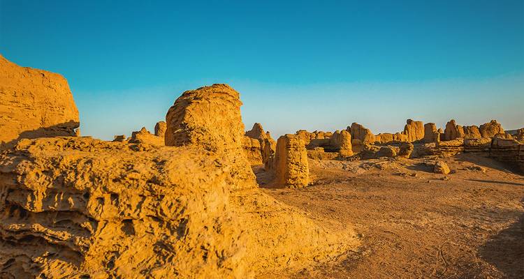 Eroded Yardang rock formations rise from a barren desert landscape under a clear blue sky.