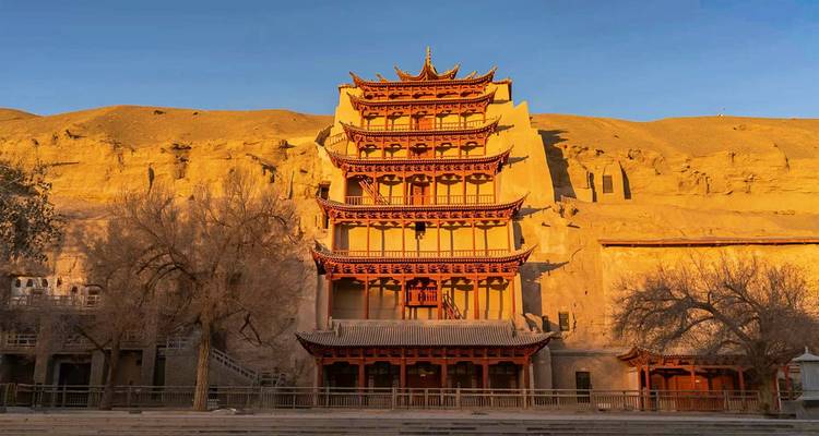 The multi-tiered facade of Mogao Caves' Nine-story Pagoda glows in soft afternoon light against cliffside.