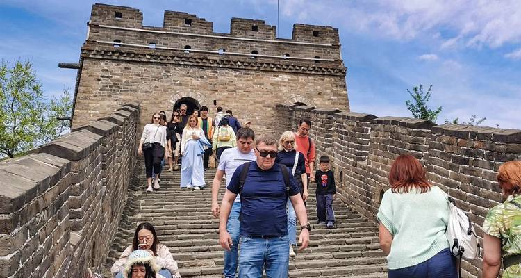 Tourists walk down a stone stairway on the Great Wall of China under a blue sky.