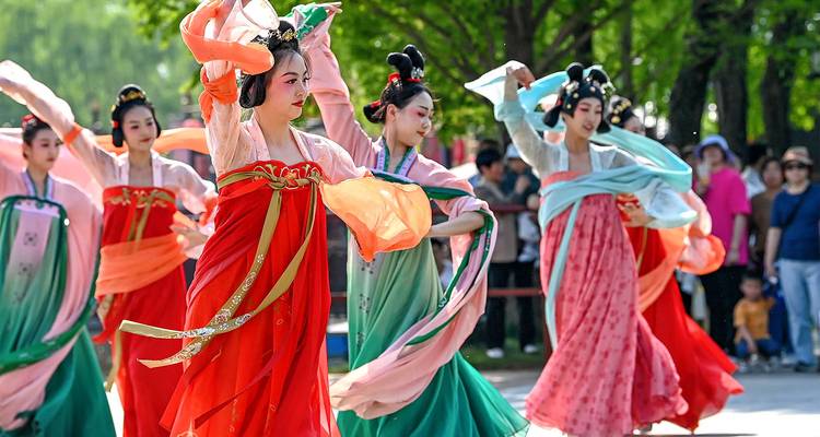 Colorful dancers in flowing traditional costumes perform an outdoor cultural show before a crowd.