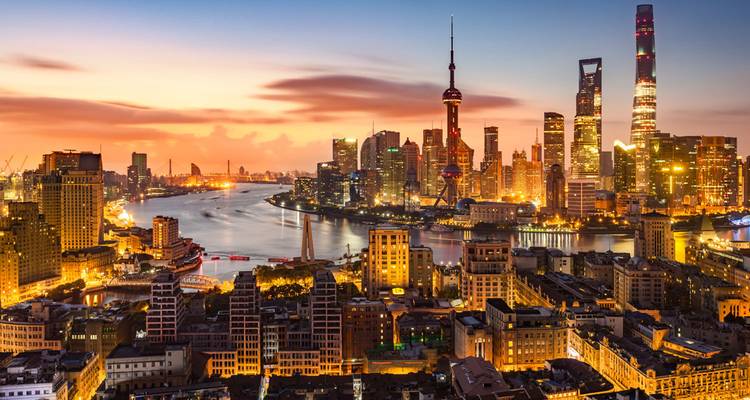 Dramatic sunset view over the Shanghai skyline and Huangpu River with illuminated skyscrapers.