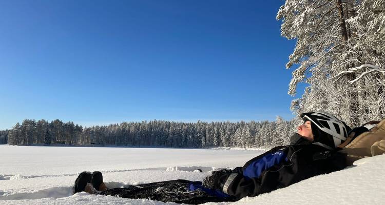 Persona relajándose en la nieve bajo un cielo azul despejado.