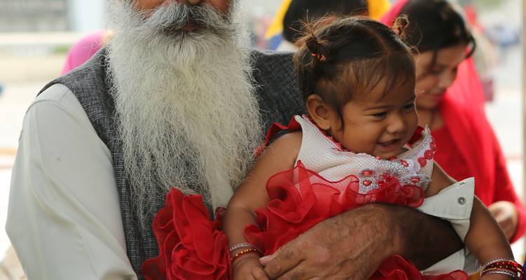 Un homme barbu tenant un petit enfant dans une robe rouge, souriant.