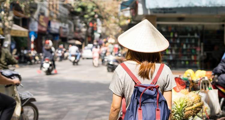 Frau, die durch einen belebten Straßenmarkt geht und einen traditionellen Hut trägt.