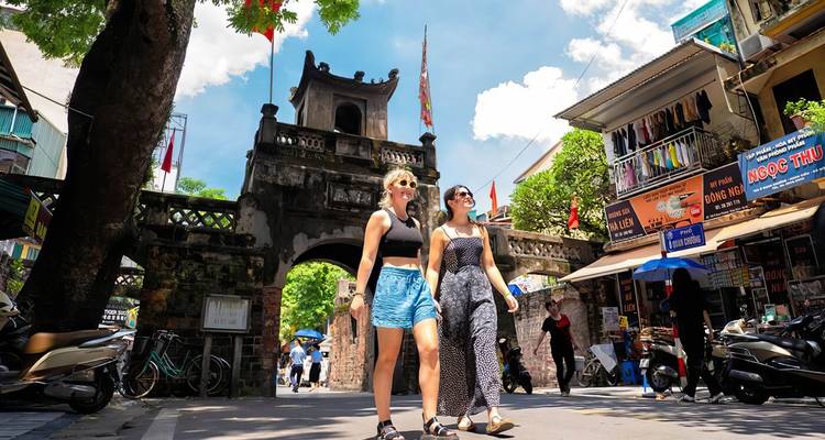 Zwei Frauen schlendern durch einen belebten vietnamesischen Straßenmarkt.