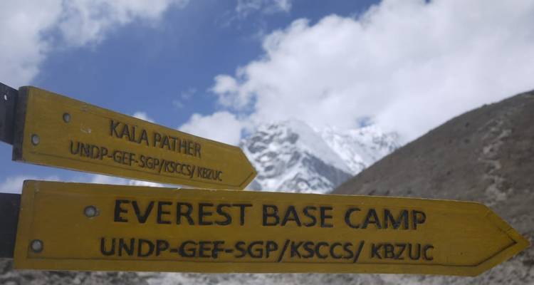 Gele wegwijzers die naar Kala Patthar en Everest Base Camp wijzen met besneeuwde bergtoppen op de achtergrond