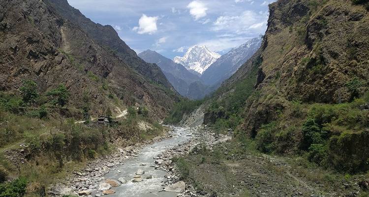 Steep Himalayan valley with a rocky river and snow-covered peaks under a bright sky