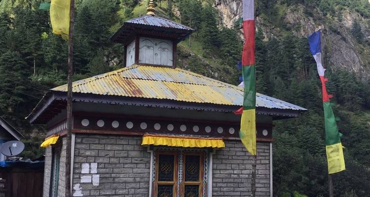 Small stone shrine with prayer flags set against forested cliffs