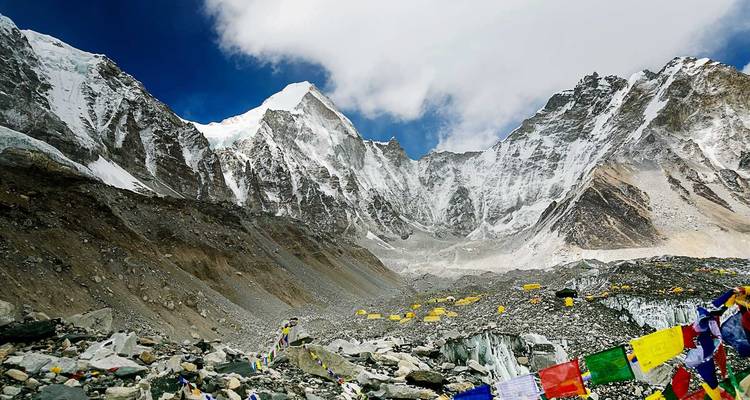 Everest Base Camp area with towering icy peaks, prayer flags and yellow expedition tents on the glacier