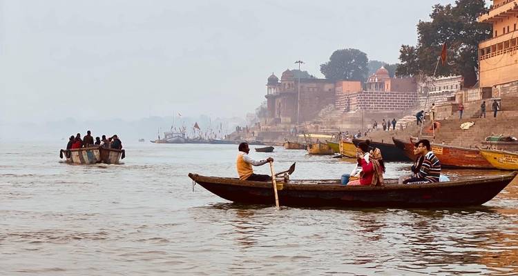 Des gens dans de petites embarcations explorant le fleuve Gange avec ses ghats historiques.