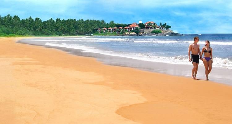 Ein Paar, das an einem unberührten Sandstrand mit ruhigen Wellen entlanggeht.