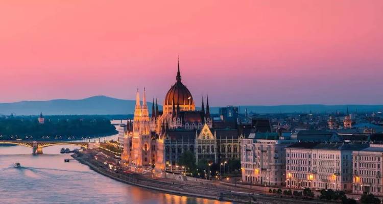 Das beleuchtete Parlamentsgebäude von Budapest und die Skyline am Fluss in rosa Sonnenuntergang über der Donau.