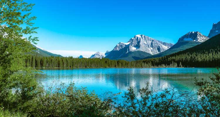 Crystal-clear turquoise lake reflecting snow-capped peaks and dense evergreens in the Canadian Rockies.