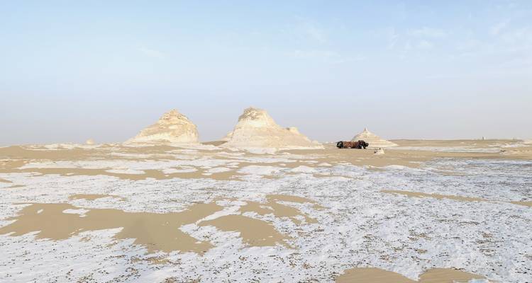Escena del desierto con formaciones rocosas y un vehículo en la distancia.