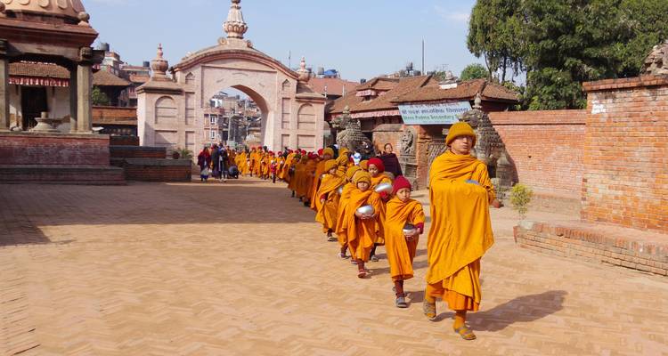 Monjes vestidos con túnicas naranjas caminando en fila en un complejo histórico.