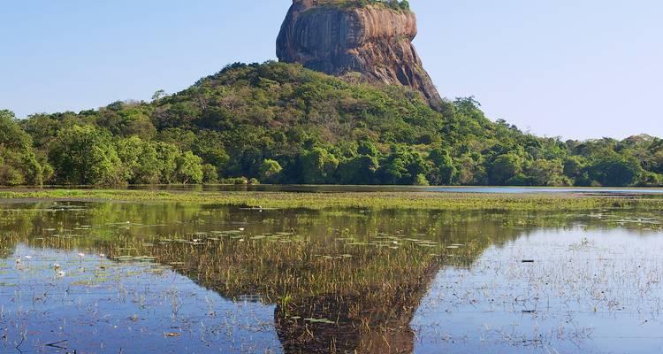 Scenic view of Sigiriya Rock with reflection in the water surrounded by lush greenery.