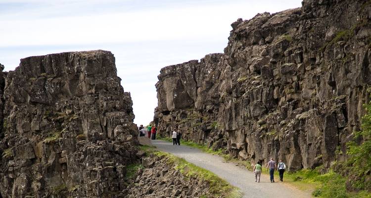 Visitantes caminando por un valle de grieta rocoso a lo largo de un sendero de grava en el Parque Nacional de Þingvellir.