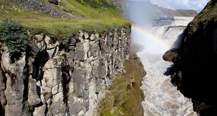 Una poderosa cascada que se desploma a través de un estrecho cañón rocoso con un arcoíris brillante en la niebla.